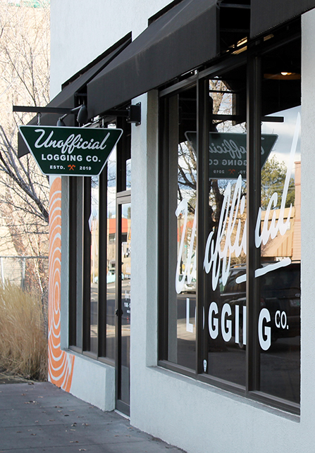 The shop front features a hanging sign and logo in addition to the logo painted on the large glass storefront windows